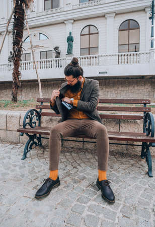 Young handsome hipster man sitting on a wooden bench in the cityの写真素材