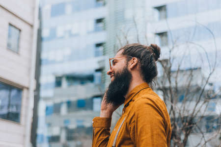 Young handsome hipster man holding a coat during business call on mobileの写真素材