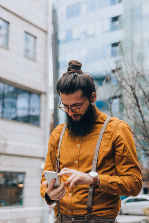 Young caucasian guy clothed in a fashionable costume using his mobile phoneの写真素材