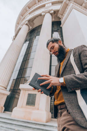 A handsome young hipster guy reading a book in an urban environment
