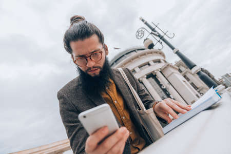 Young caucasian guy clothed in a fashionable costume using his mobile phoneの写真素材