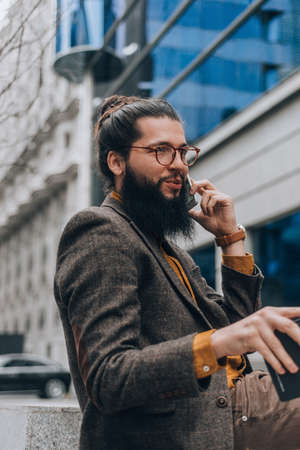 Stylish caucasian male clothed in a fashionable outfit making a phone call outdoorsの写真素材