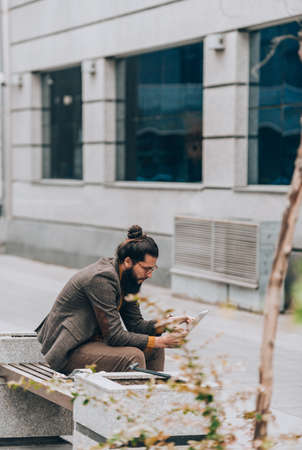 A handsome young guy dressed in modern clothes holding a tablet in an urban environmentの写真素材
