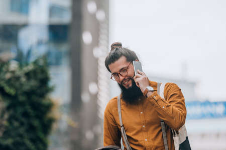 Modern day young businessman with long hair and beard at the promenade talking on cellphoneの写真素材
