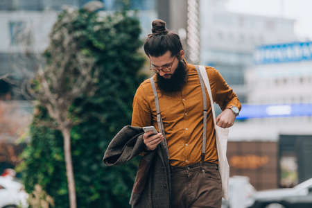 Fashionable male wearing stylish modern clothing holding a phone at the city squareの写真素材