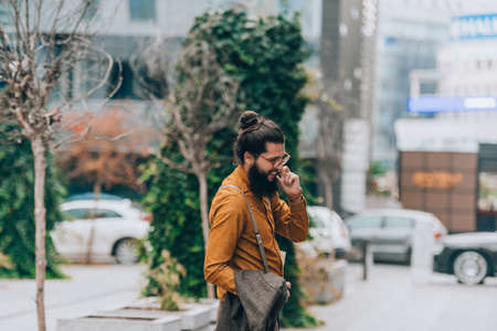 Young handsome hipster man holding a coat during business call on mobileの写真素材