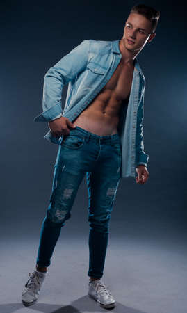 Portrait of a handsome male model posing while taking off his shirt against dark backgroundの写真素材