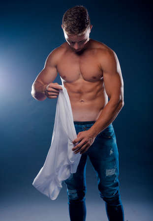 portrait of a happy smiling young man taking off his shirt isolated against dark backgroundの写真素材