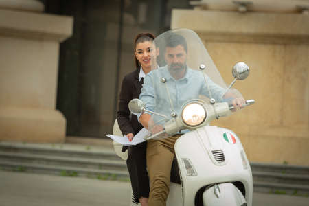 Two italian business peopel are riding the motorcycle while smiling