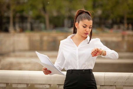 Attractive businesswoman is checking the time while holding the documents in her hands