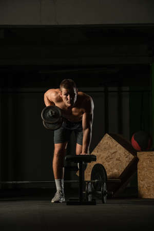Sportsman doing exercises with weights over fitness bench and looking straight at the camera.の写真素材