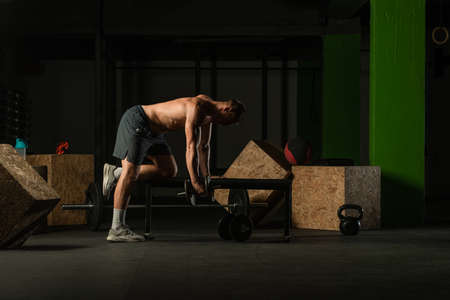Athletic caucasian man doing a dumbbell triceps kickback with his right arm on a horizontal bench.