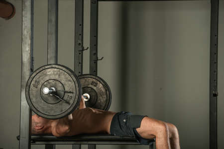 Athletic muscular bodybuilder doing bench press workout indoors in a modern gym.