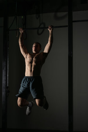 Handsome bodybuilder doing pull-ups on horizontal bar in a indoors modern gym.