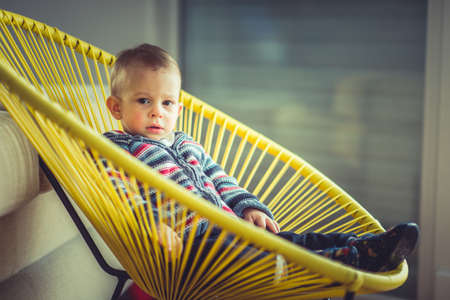 A sweet baby boy is looking serious while sitting in a beautiful chair