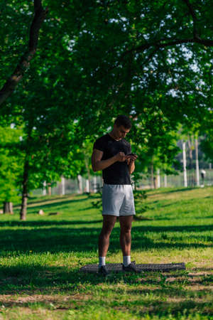 Athletic sportsman checking his phone while taking a break from a workout in the parkの写真素材