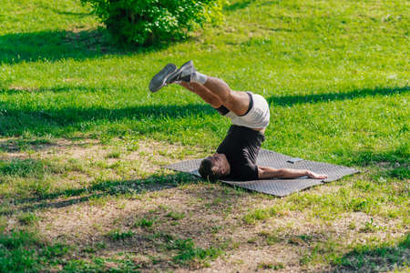 Young sporty handsome man practicing yoga in the park and doing the plow pose.の写真素材