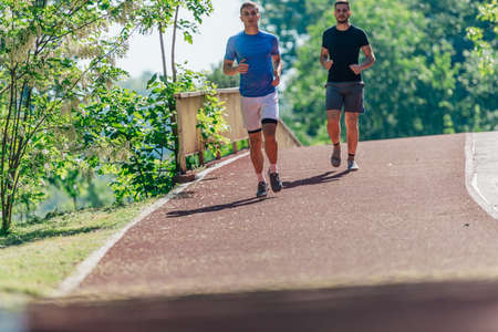Two young male friends are running through the forest on a jogging trailの写真素材