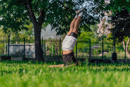 Young sporty handsome man practicing yoga in the park and doing the plow pose.