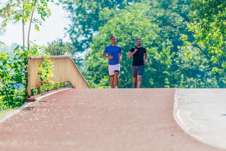 Two young male friends are running through the forest on a jogging trail