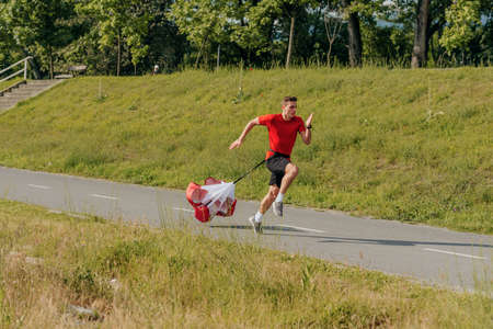 Side view of a strong man doing workout using resistance parachute outdoors