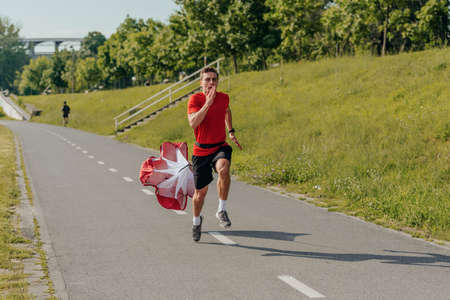 Male athlete wearing a red t-shirt is running with a parachute in the park