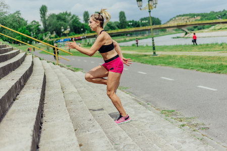 Fit healthy athlete, beautiful woman in tight sportswear jumping on stairs, warming up before jogging while looking highly motivated.の写真素材