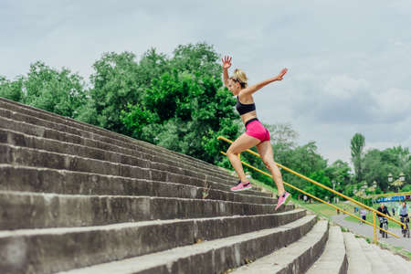 Fit healthy athlete, beautiful woman in tight sportswear jumping on stairs, warming up before jogging while looking highly motivated.の写真素材