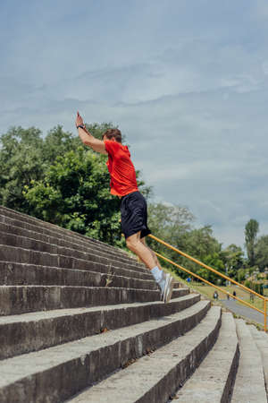 Side view picture of an active male athlete jumping up on stairs in outdoor training.