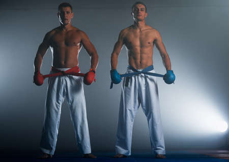 Strong fit athlete, karate men or fighters in white kimono, suit, with belt posing in fighting stanceの写真素材