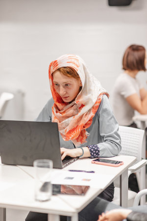 Ginger woman in hijab working on lap top