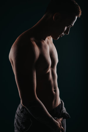 Fit man flexing muscles, showing results of body transformation, on black background. Athlete silhouette inspires motivation.の写真素材