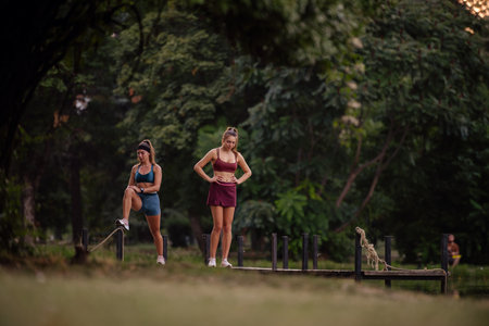 Fit girls exercising and warming up outdoors in a green park. Athletic females stretching on a bridge, preparing for a cardio workout.の写真素材