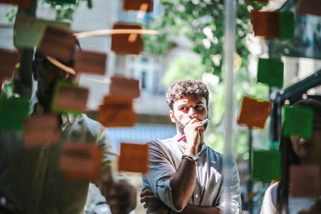 Diverse people collaborate in a modern office, sharing ideas on a glass board. They strategize, set goals, and work persistently to achieve success.の写真素材