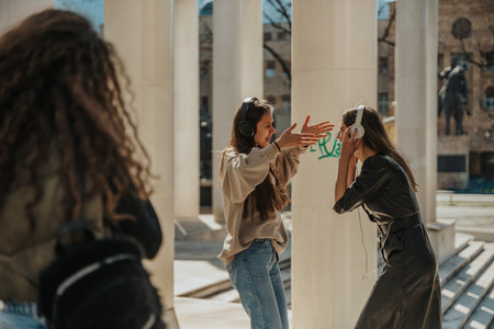 Curly haired girl is taking a photo of her two brunette friends while they are listening to music on their headphones, dancing and looking at each otherの写真素材