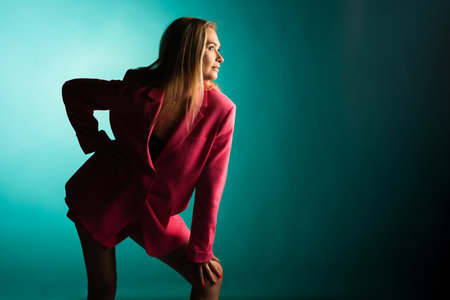 Confident Young Lady Posing in Studio with Gorgeous Pink Jacket on Turquoise Backgroundの写真素材