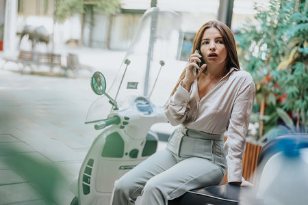 Businesswoman on a scooter, having a phone call and discussing work. She plans project costs and...