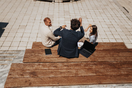 Working remotely in the city. Business people sitting on bench in urban area discussing statistics on tablet, working in positive atmosphereの写真素材
