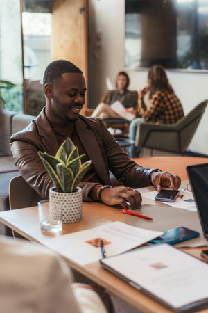 Smiley handsome black male person sitting on meeting table working with his coworkersの写真素材