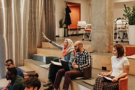 Woman in hijab raising hand to ask question during business training at small amphitheater in business centerの写真素材