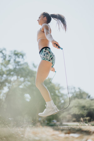 Woman exercising outdoors in a sunny park. She jump rope, stretch, and warm up. Her fit body display their dedication to a healthy lifestyle.の写真素材
