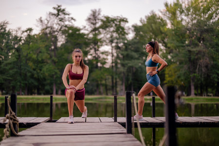 Fit women warm up, stretching on a park bridge. They exercise outdoors, demonstrating strength and...