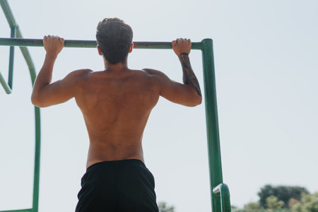 Caucasian friends exercising outdoors in a park, doing pull-ups on metal bars. Fit bodies, motivation, and persistence in their fitness routine.の写真素材