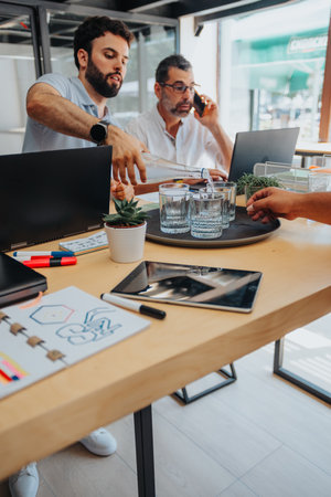 Male employee pouring water in glasses for his teammates while working together at the office.