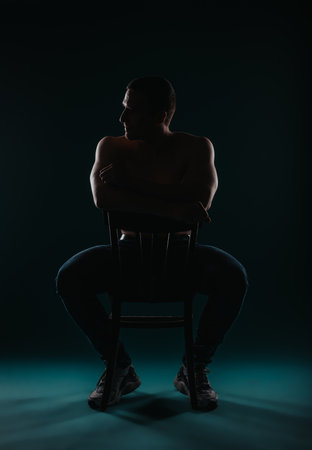 Fit, shirtless man looking aside while sitting on a chair. Fit sports person posing.の写真素材