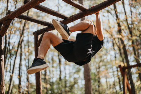 A man does pull ups outdoors in a forest. He enjoys a sunny day hiking, surrounded by trees.の写真素材