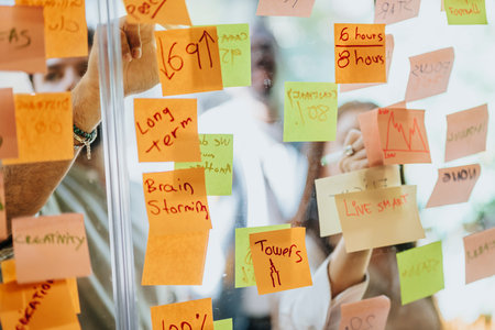 Sticky notes cover a glass wall as creative people share ideas for successful teamwork and strategic planning.の写真素材