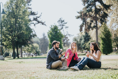 Young friends having fun, eating ice cream and laughing in a city park. Enjoying nature, socializing, and embracing carefree moments on a sunny day.の写真素材