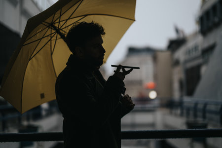 Businessman having phone call while holding umbrella on a rainy day.の写真素材