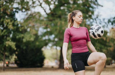 An athletic girl has fun training outdoors, playing soccer and performing freestyle tricks on a sunny day surrounded by trees.の写真素材
